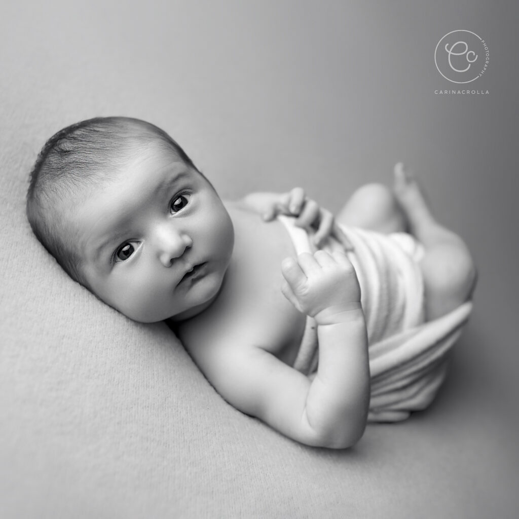 A black and white photo of a newborn baby laying on it's back looking at you. Best Time For Newborn Photos